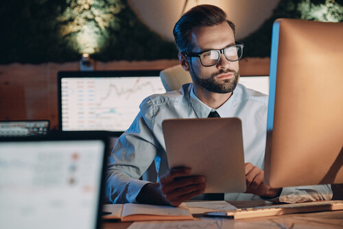 Foto de um homem concentrado olhando para um computador e com um tablet na mão para ilustrar o serviço da Digicloud de Digitalização de documentos